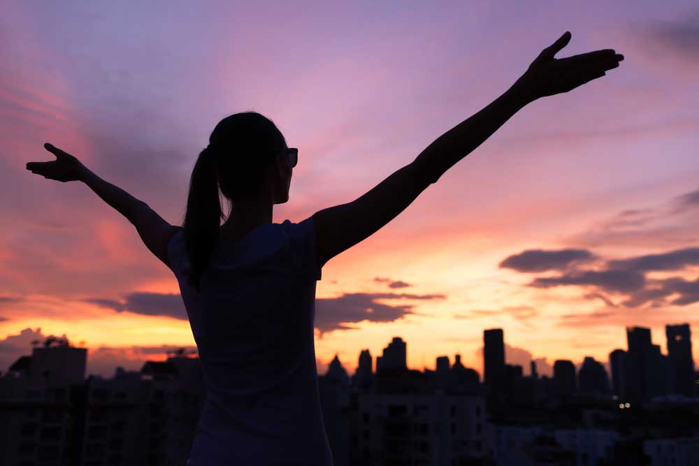 woman with outstretched arms overlooking a cityline at sunset - life after drug rehab - summit bhc addiction and alcohol treatment centers across the united states 